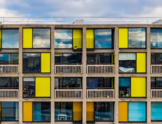 Park Hill Phase One - A concrete framed building with large glass windows, concrete balconies and brightly coloured yellow and orange metal panels