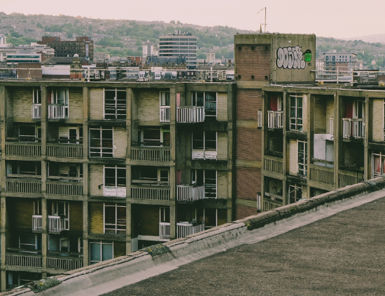 Derelict building with broken windows and doors, some of them boarded up, concrete damaged and graffiti on the walls